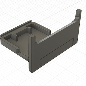 Peut inclure: Un objet gris foncé imprimé en 3D, avec une base rectangulaire et un support vertical incliné. La conception comprend une zone encastrée et une fente, suggérant un support fonctionnel pour composants électroniques.