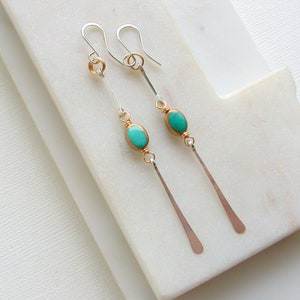 May include: A pair of long, silver dangle earrings with turquoise oval-shaped stones and gold accents.