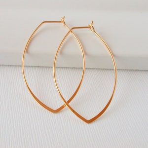 May include: A pair of gold-toned, open hoop earrings with a slightly pointed, oval shape.