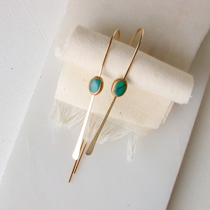 May include: A pair of gold earrings with turquoise stones. The earrings are long and thin, with a simple design.