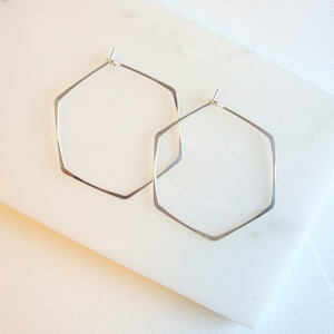 May include: A pair of silver hexagonal hoop earrings. The earrings are simple and elegant, and would make a great addition to any jewelry collection.