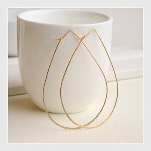 May include: A pair of gold teardrop-shaped hoop earrings. The earrings are made of thin wire and are simple and elegant.