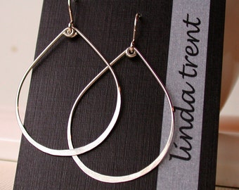 May include: A pair of silver teardrop-shaped hoop earrings on a black card with the text "linda trent" printed on it.
