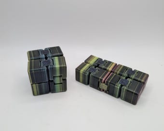 Puede incluir: Dos cubos infinitos multicolores se muestran sobre un fondo blanco. Los cubos están hechos de pequeños bloques rectangulares en tonos de negro, verde y rosa. Un cubo tiene forma de cubo, y el otro está en línea recta.