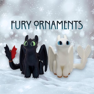 May include: Two dragon ornaments, one black with green eyes and red accents, the other white with blue eyes. The text "FURY ORNAMENTS" is displayed above the ornaments against a snowy background.