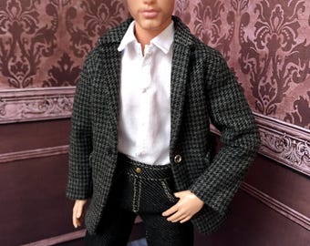 Pode incluir: Boneco vestindo um blazer pied-de-poule preto e branco sobre uma camisa branca com gola, combinado com calças jeans pretas. O boneco tem cabelo loiro e posa em frente a uma parede estampada. O blazer tem dois botões dourados.