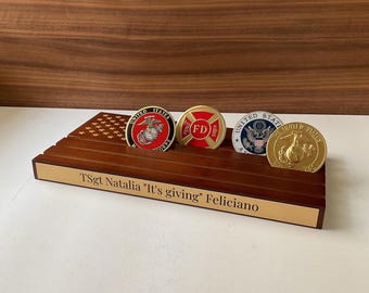May include: A wooden coin display case with an American flag design. The case holds four challenge coins with various designs, including a fire department logo, a United States Marine Corps logo, and a United States seal. The case is engraved with the text "TSgt Natalia "It's giving" Feliciano".
