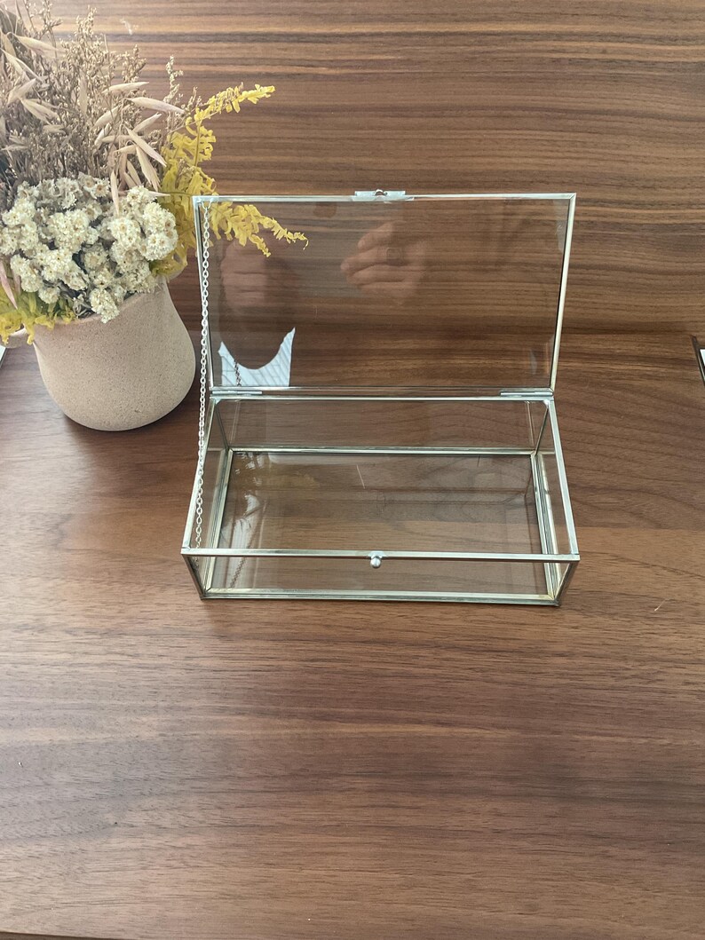 May include: A clear glass box with a silver metal frame and a hinged lid. The box is open and the lid is propped up.