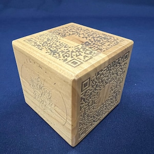 May include: A wooden box with a QR code on each side. The box is made of light brown wood and has a natural finish. The QR codes are laser engraved into the wood.
