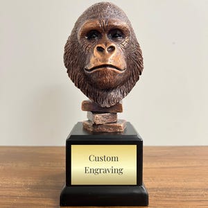 May include: A bronze gorilla head sculpture on a black base with a gold plaque that says "Custom Engraving".