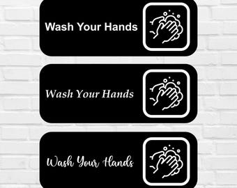 May include: Three black rectangular signs with rounded corners are stacked vertically. Each sign has the words "Wash Your Hands" in white, with a white graphic of hands washing with soap in a square box.