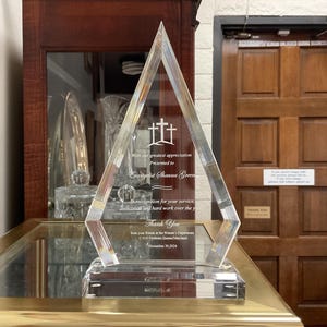 Op de afbeelding: Een heldere glazen award in de vorm van een diamant met een inscriptie die luidt: "Met onze grootste waardering Gepresenteerd aan Evangelist Shauna Green - Ter erkenning voor uw dienst, toewijding en hard werken door de jaren heen Dank u van uw vrienden van de vrouwenafdeling, COG Firths, Queen Maryland 30 november 2024"