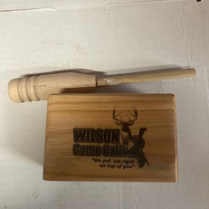 May include: A wooden box with a deer and turkey design and the text "Wilson Game Calls" and "We put 'em right on top of you".