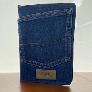 May include: A blue denim notebook with a large back pocket and a brown leather patch featuring a dog silhouette and the text "1912".