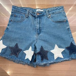 May include: Blue denim shorts with a frayed hem and a row of white and black stars sewn on the bottom.