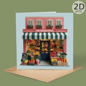 Puede incluir: Una tarjeta de felicitación con una maqueta en miniatura de una tienda de productos frescos, "The Veggie Patch". La tienda tiene una fachada rosa, un toldo a rayas verdes y blancas y una puerta azul. La tienda está llena de frutas y verduras.
