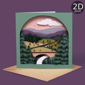 May include: A 2D print greeting card featuring a layered paper design of a train traveling through a mountain landscape. The card has a green frame, a pink sky, and a brown envelope.