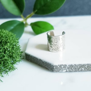 May include: Silver ear cuff with a floral design. The cuff is made of metal and has a smooth finish.