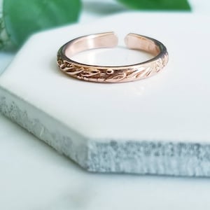 May include: A delicate rose gold ring with an intricate floral design. The ring is open and adjustable to fit most finger sizes.