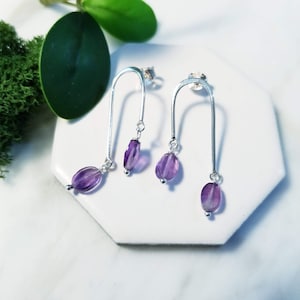 May include: A pair of silver earrings with a curved bar design and dangling amethyst stones.