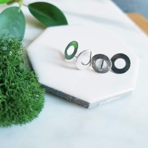 May include: Three silver-toned metal earrings with a circular shape and a hole in the centre. The earrings are arranged in a row on a white surface.