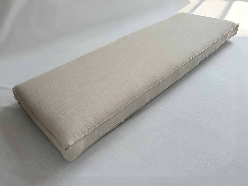 Puede incluir: Un coj&iacute;n rectangular para banco en color beige neutro. El coj&iacute;n tiene una apariencia a medida con un borde ribeteado. La tela tiene una textura sutil, que sugiere lino o un material similar. El coj&iacute;n est&aacute; dise&ntilde;ado para sentarse.