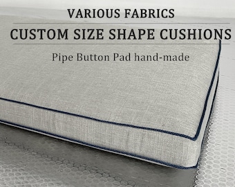 May include: A light gray custom size and shape cushion with a dark blue piping detail. The cushion is made with a linen fabric and has the text "VARIOUS FABRICS CUSTOM SIZE SHAPE CUSHIONS Pipe Button Pad hand-made" printed on the top.
