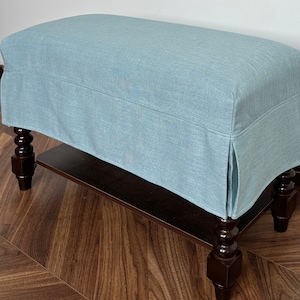 Op de afbeelding: Een lichtblauwe gestoffeerde bank met een houten frame en gedraaide poten. De bank heeft een rok en staat op een donkere houten vloer.