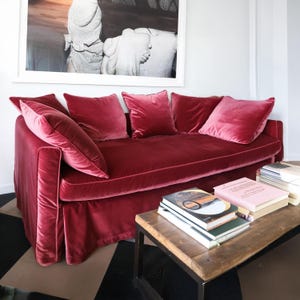 Peut inclure: Un canapé en velours rouge avec des coussins assortis. Le canapé a une base à jupe et est associé à une table basse en bois avec des livres. Une grande œuvre d'art encadrée en noir et blanc est accrochée au-dessus du canapé.