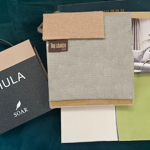 May include: A fabric swatch book with a variety of colors and textures. The book includes a sample of a light green fabric, a light brown fabric, a white fabric, and a dark green fabric. The book also includes a sample of a light gray fabric with a brown trim. The book is labeled "Top Choice Textile".