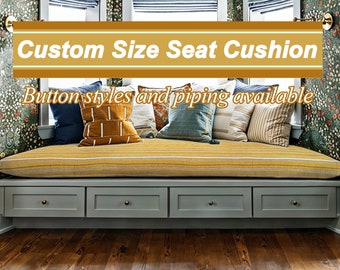 Puede incluir: Un cojín de asiento de ventana de tamaño personalizado con tela a rayas amarilla y blanca. El cojín se coloca en un asiento de ventana gris con tres cajones. El texto "Custom Size Seat Cushion" y "Button styles and piping available" se muestra sobre el cojín.