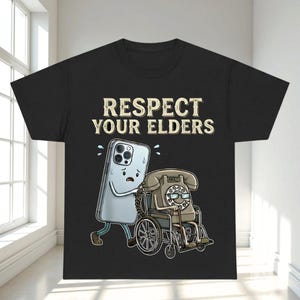 a black t-shirt with a graphic design depicting a phone character pushing a wheelchair-bound character. The text on the t-shirt reads "RESPECT YOUR ELDERS".