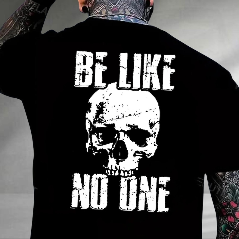 May include: Black t-shirt with a white skull graphic and the text "BE LIKE NO ONE". The skull graphic is centered and has a distressed, textured appearance. The text is in a bold, uppercase font.