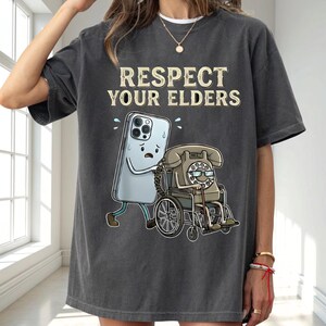 a person wearing a gray t-shirt with a graphic design depicting a phone character pushing a wheelchair with a person in a wheelchair.