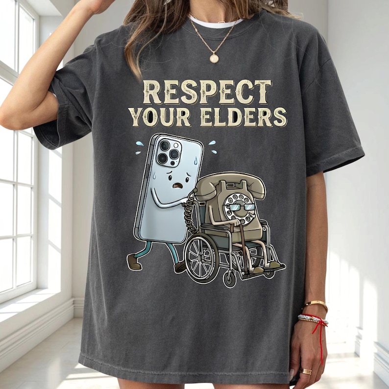 a person wearing a gray t-shirt with a graphic design depicting a phone character pushing a wheelchair with a person in a wheelchair.