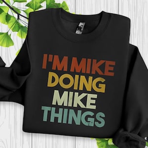 May include: Black sweatshirt with the text "I'M MIKE DOING MIKE THINGS" in orange, yellow, and teal lettering. The sweatshirt is a crew neck style.
