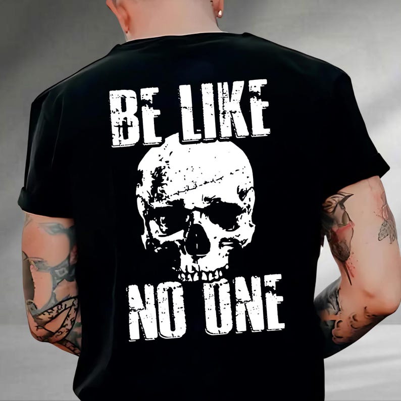 May include: Black t-shirt with a white skull graphic and the text "BE LIKE NO ONE". The design features a distressed, vintage style. The shirt is a classic crew neck.
