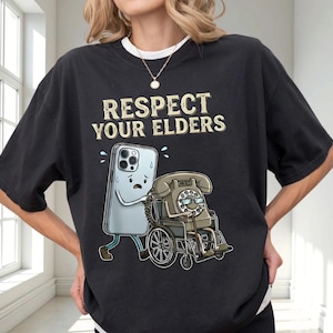 A person wearing a black t-shirt with a graphic design depicting a phone and a wheelchair, along with the text "RESPECT YOUR ELDERS".