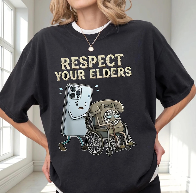 A person wearing a black t-shirt with a graphic design depicting a phone and a wheelchair, along with the text "RESPECT YOUR ELDERS".