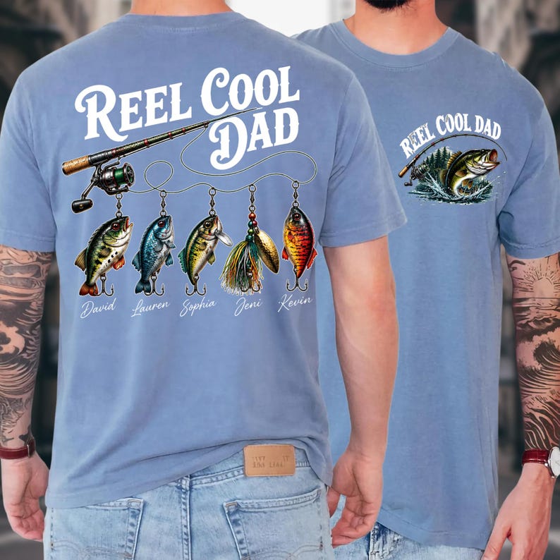 A man wearing a blue t-shirt with a fishing-themed design and text that says "Reel Cool Dad".