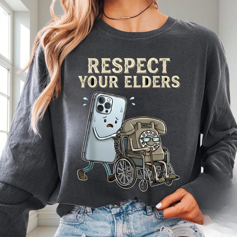a person wearing a gray sweatshirt with a graphic design depicting a phone character pushing a wheelchair with a dial.