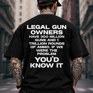 May include: A black short-sleeved t-shirt featuring white text on the back that reads: LEGAL GUN OWNERS HAVE 300 MILLION GUNS AND 1 TRILLION ROUNDS OF AMMO. IF WE WERE THE PROBLEM YOU'D KNOW IT. The shirt has a crew neckline and a loose fit.