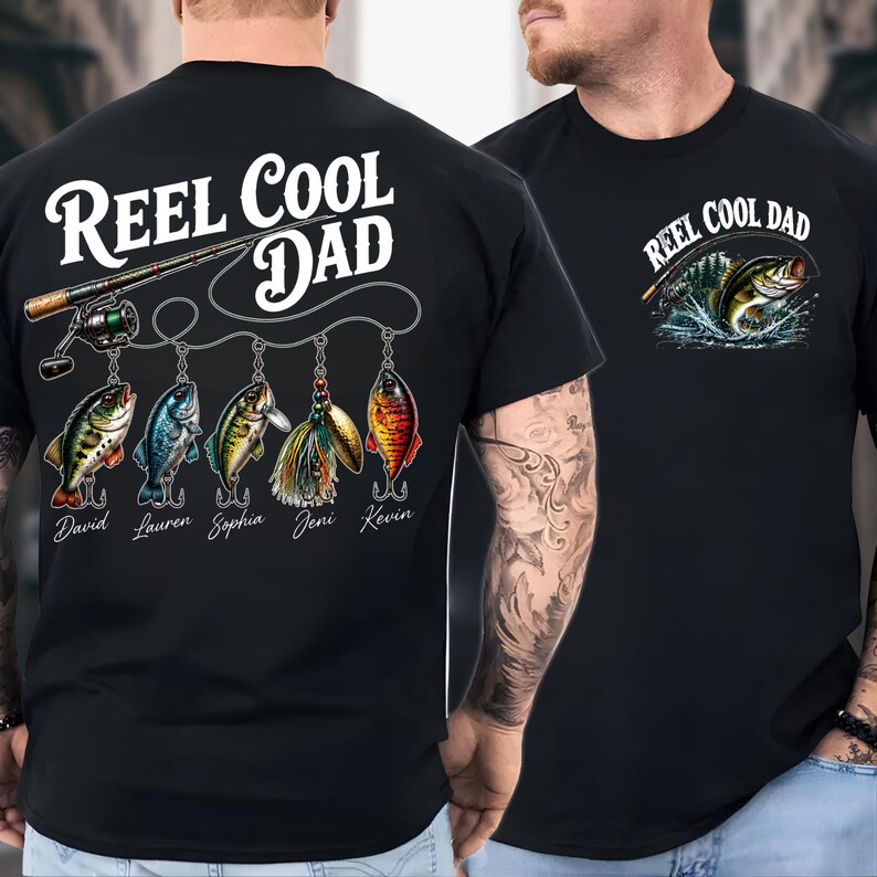 a black t-shirt with a design that includes a fishing rod, fish, and the text "Reel Cool Dad" printed on it.