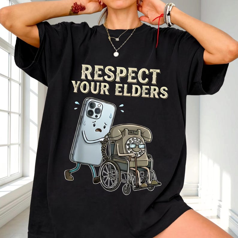 A person wearing a black t-shirt with a graphic design depicting a phone and a wheelchair, along with the text "RESPECT YOUR ELDERS".