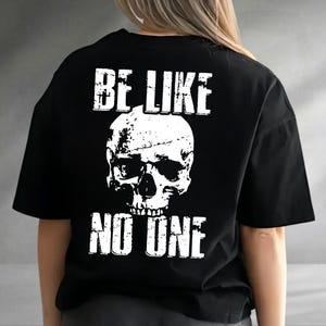 May include: Black t-shirt with a distressed white skull graphic and the text "BE LIKE NO ONE". The design is centered on the back of the shirt. The shirt has short sleeves and a crew neck.