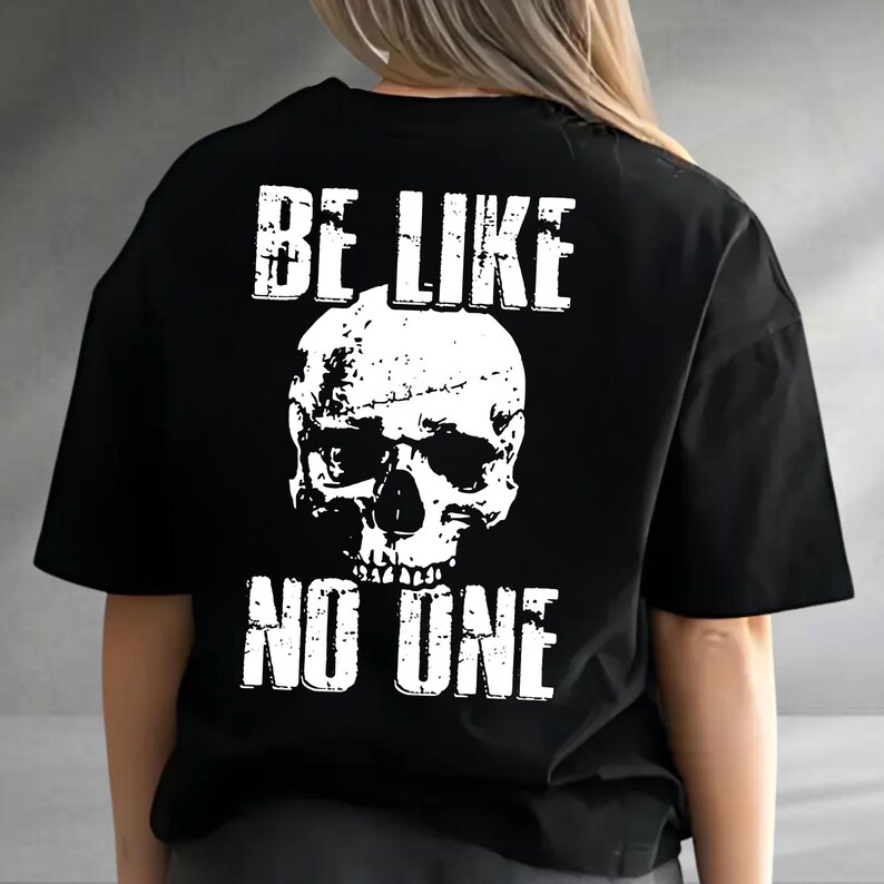 May include: Black t-shirt with a distressed white skull graphic and the text "BE LIKE NO ONE". The design is centered on the back of the shirt. The shirt has short sleeves and a crew neck.