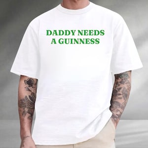 A person wearing a white t-shirt with the text "DADDY NEEDS A GUINNESS" printed on it.