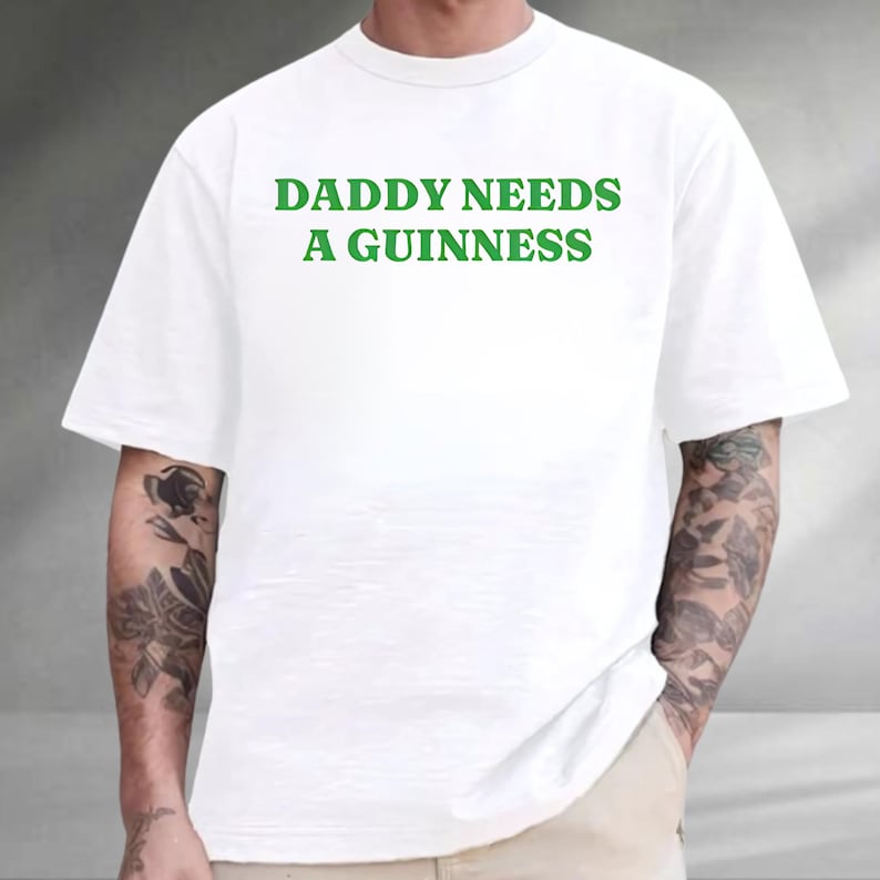 A person wearing a white t-shirt with the text "DADDY NEEDS A GUINNESS" printed on it.