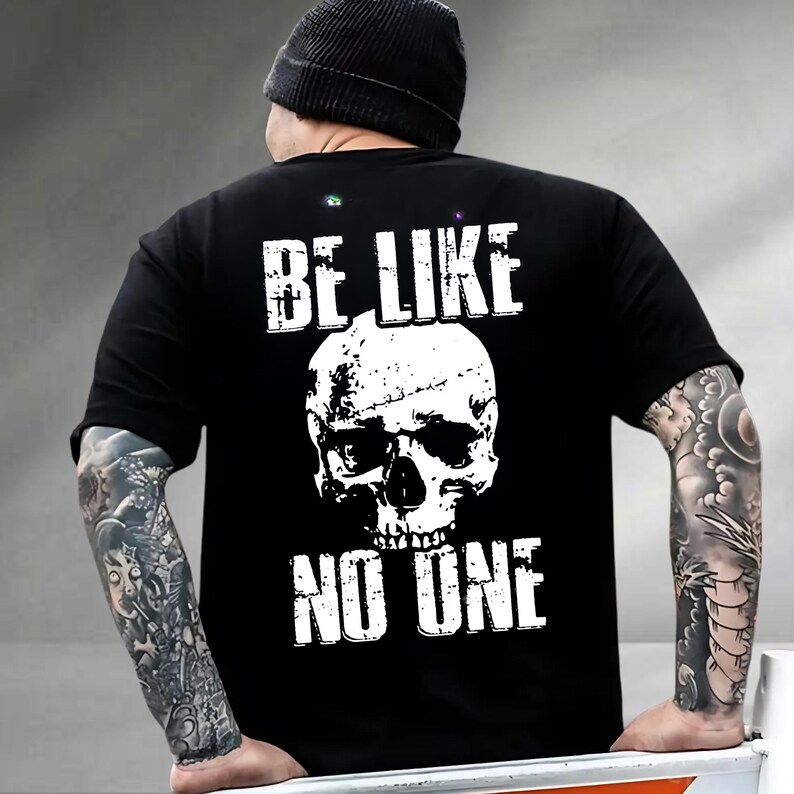 May include: Black t-shirt with a white skull graphic and the text "BE LIKE NO ONE". The design is centered on the back of the shirt. The shirt is made of a soft material.