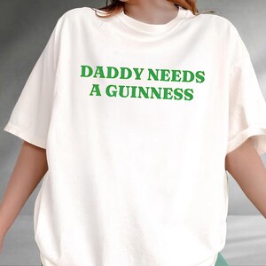 A person wearing a white t-shirt with the text "DADDY NEEDS A GUINNESS" printed on it.